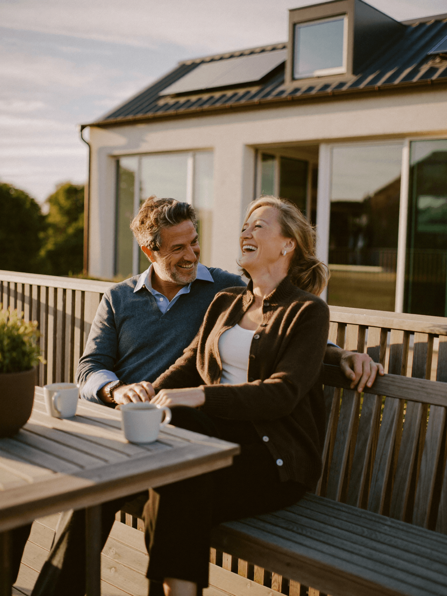 Tevreden huiseigenaren genieten op hun terras, met zonnepanelen op het dak van hun woning